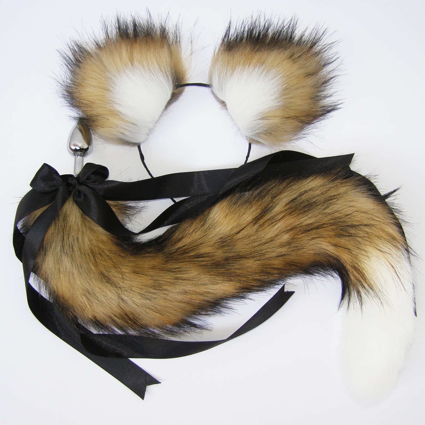 A brown and white faux fur cat tail butt plug with a stainless steel plug and a black ribbon attached.
