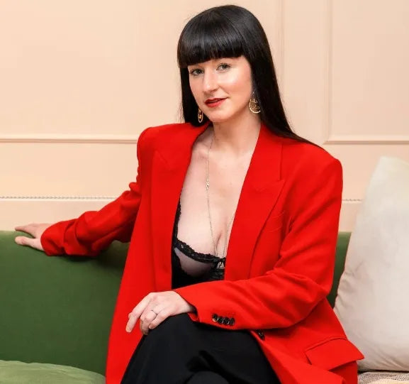 Woman wearing a red blazer over a black top on a green couch.